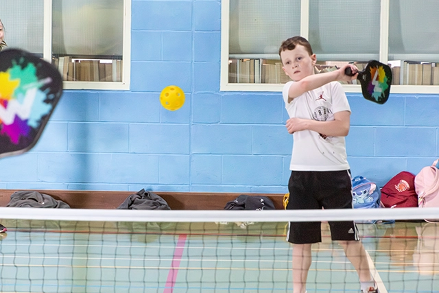 Youth Pickleball Children playing pickleball indoors with a yellow ball.