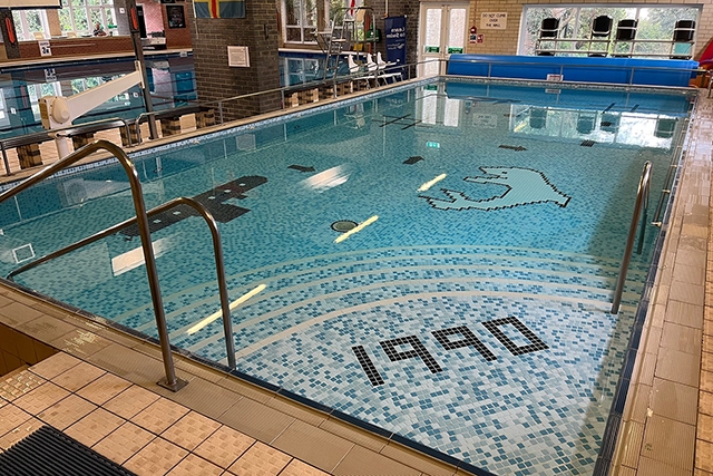 Learner Pool This is a photo of an indoor swimming pool with blue tiled steps that spell out "1990". The pool also has a pixelated dolphin graphic at the bottom.